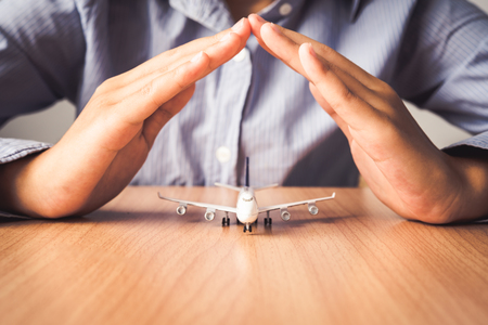 Hand protecting the icon a plane - the concept of insurance for travelの写真素材
