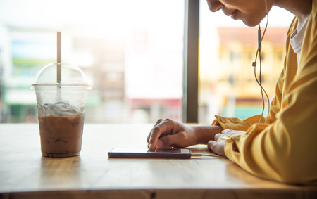 The girl is enjoying the phone in coffee cafe and have a glass of cold drink in a foregroundの写真素材