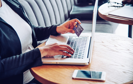 Hand holding a credit card in their hands and find information about a product using their laptop device to make purchases online and conduct financial transactions.の写真素材