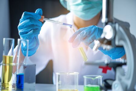 closeup-pipette dropping a sample into a test tube in an experiment research in laboratory.