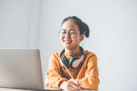 Teenage Asian students in a yellow dress wearing a headphone are communicating through video...
