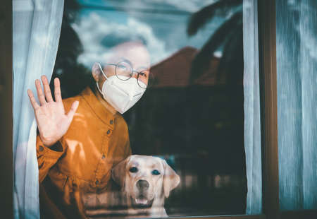 Asian girl wearing glasses, wearing a mask, with Labrador dog looking out the window, is bored of...
