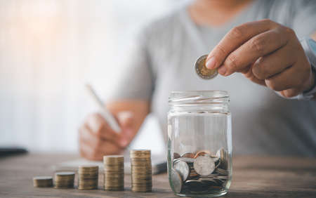 hand holding coins to put the glass piggy bank. Saving and financial accounts concept
