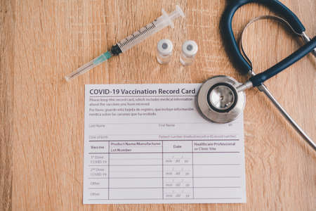 Coronavirus vaccination record card is placed on a wooden floor with a vaccine syringe and a stethoscope.patient who has already been vaccinated with Coronavirus .Coronavirus preventionの写真素材