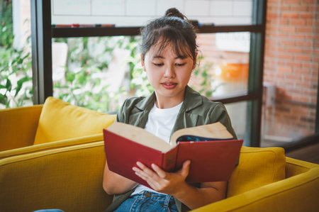 female college student is reading a book in a cafe during the day.の写真素材