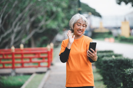 Elderly white haired Asian woman talking Video call while exercising in the park in the morning.の写真素材