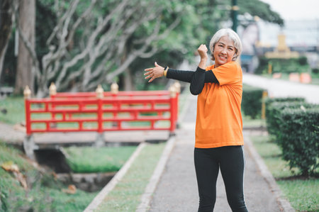 Elderly, white-haired Asian woman exercising in the park early in the morning.の写真素材