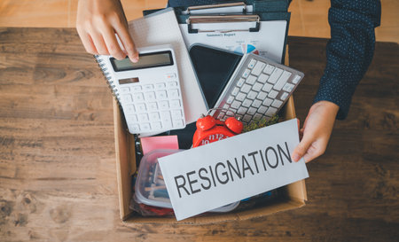 Female company employee packing office supplies and personal items in cardboard boxes before leaving...