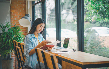 female college student is reading a book in a cafe during the day.の写真素材