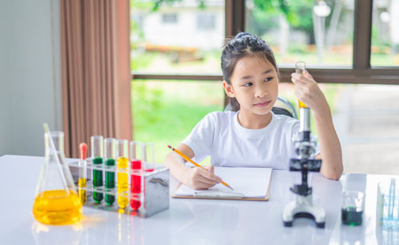 little scientist looking through a microscope and test tubes filled with chemicals for learning about science and experiments.の写真素材