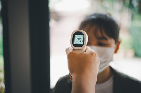 Hand holding infrared thermometer to measuring temperature  people with face mask on background. Covid flu screening 19 concept.の写真素材