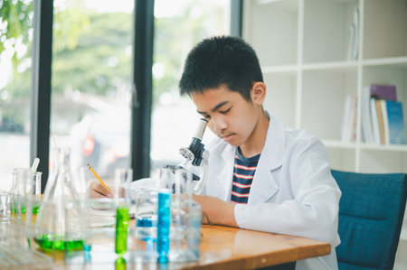 Asian male science students looking through a microscope and tests of plants in the classroom. Learning about scientific experiments on plant species.の写真素材