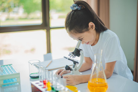 little scientist looking through a microscope and test tubes filled with chemicals for learning about science and experiments.の写真素材
