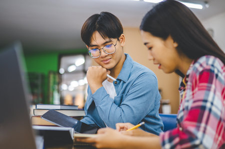Students are consulting each other working on laptops and searching for books to study, make...