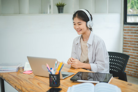Teenage Asian students  wearing a headphone are communicating through video conferencing for online learning. In a video Teenage Asian students  wearing a headphone are communicating through video conferencing for online learning. In a video conference call via apps.の写真素材