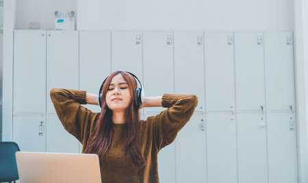 young student wearing headphones is relaxing during long online classes, distance learning, and keeps up to date on the global coronavirus pandemic.の写真素材