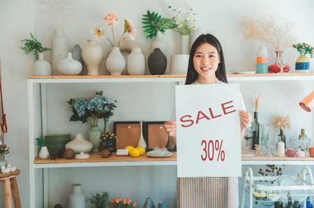 Smiling online small business owner holding a sign saying sale 30% and happily working at a courier...
