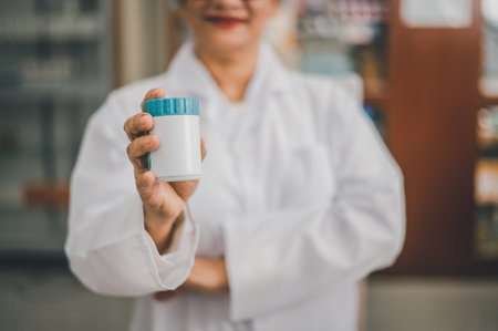 close up pharmacist hand holding pill bottle sticking out to introduce products Medicine, Drugs, Vitamins, in modern pharmacyの写真素材