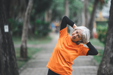 Elderly, white-haired Asian woman exercising in the park early in the morning.