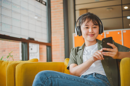 teenage woman wearing headphones sits on her phone while listening to music, playing games, ordering...