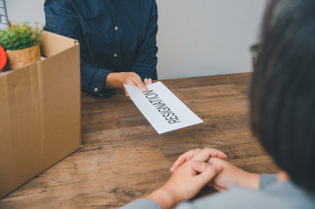 female company employee hands a white envelope with a resignation letter inside to her boss or HR before leaving her workplace.の写真素材