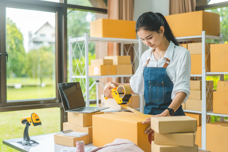 Startup small business owners holding packing machine and sealing cardboard boxes with tape to...