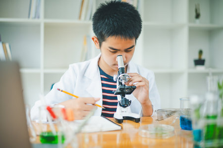 Asian male science students looking through a microscope and tests of plants in the classroom. Learning about scientific experiments on plant species.の写真素材