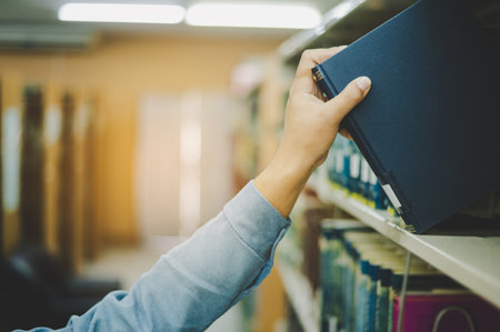 Close-up of hand picking up book on bookshelf in library to go to study.back to school conceptの写真素材