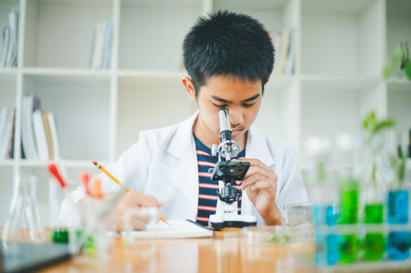 Asian male science students looking through a microscope and tests of plants in the classroom. Learning about scientific experiments on plant species.の写真素材