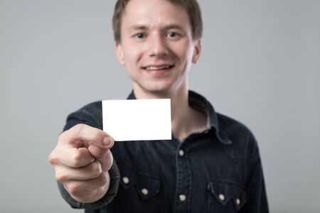 Young man showing white empty paper card on grey backgroundの写真素材