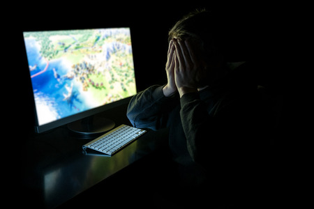 Young man playing computer games in dark room