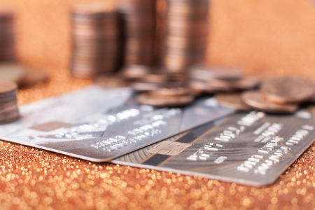 Stacks of coins and bank cards on golden sparkle background. Financial concept