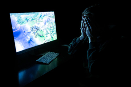 Young man playing computer games in dark room