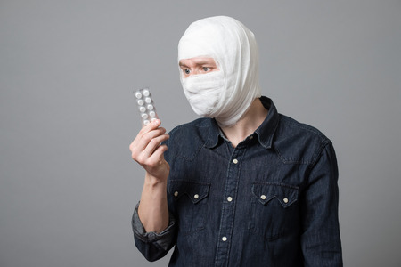 Bandaged young man holding blister pack of painkiller pills. Image related with treatment of the wounds, plastic surgery, healthcare industryの写真素材