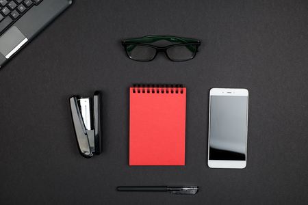 Top view of office supplies with black laptop and smartphone on surface of dark table