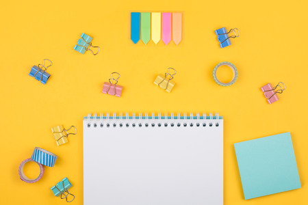 Multicolored office supplies and blank notepad  laying on yellow background top view. Creative set...