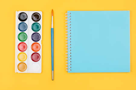 Multicolored set of pencils, watercolor and notepad laying on yellow background top view. Creative set for hobbyの写真素材
