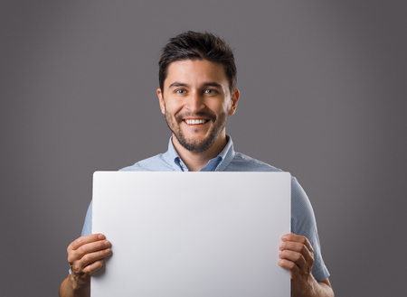 Young handsome brunet man holding white empty board. Ceo showing poster for advertisingの写真素材