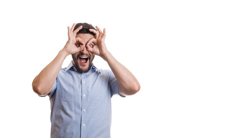 Young cheerful man with beard in blue casual shirt showing pilot goggles by fingers