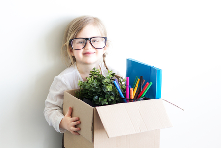 Smart little girl wearing business clothes and glasses, holding the box with documents and her stuff working in the office. Business concept.の写真素材