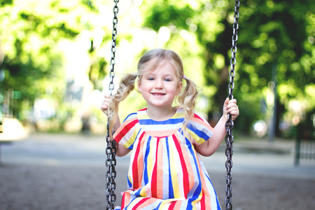 Happy child girl laughing and swinging on a swing at the play ground in summer.の写真素材