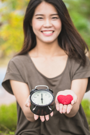 giving love and time in valentine's day. Asian women hand show red heart and clock times at 6 o'clock, It's time to loving together.の写真素材