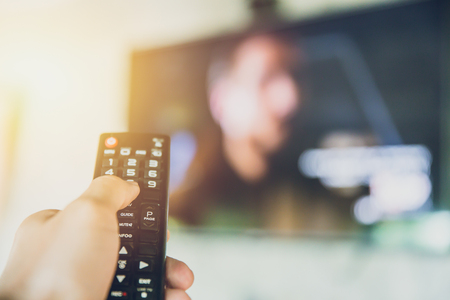 hand hold Smart TV remote control with a television blur background. change watching program channelの写真素材