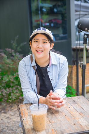 portrait cute young innocent asian teen smile sitting at the cafe with ice coffeeの写真素材