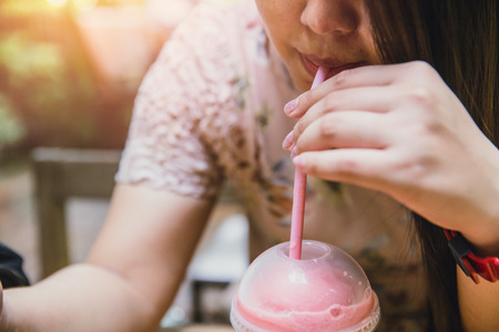 closeup women drinking cool ice smoothie fruit pink strawberry with straw in hot summerの写真素材