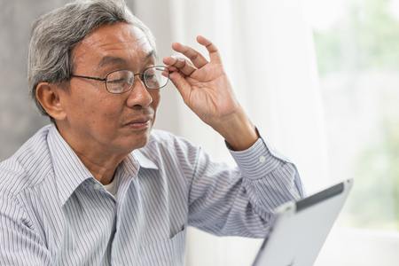 Asian glasses elderly old man happy using looking at Tablet screen to communication with other.の写真素材