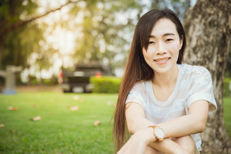 Closeup Asian teen chinese race single eyelid long hair sitting smile with dimples cheek in the parkの写真素材