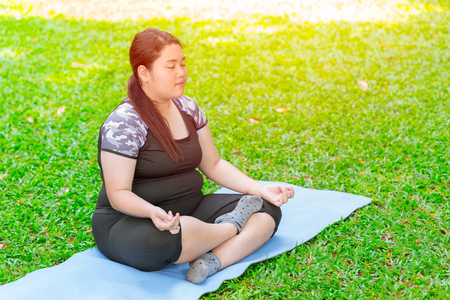 Asian fat plus size girl sitting Yoga on mat in the green garden parkの写真素材
