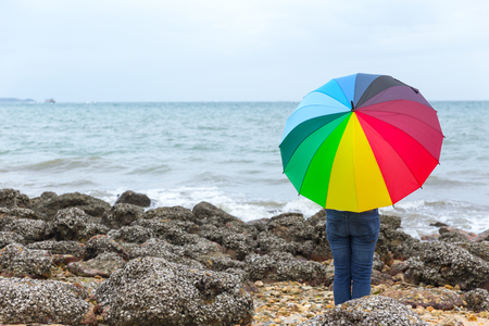 people with rainbow umbrella at the seashore stone reefの写真素材