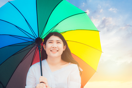 Cute Asian teen happy smile outdoor with rainbow colorful umbrella sunny dayの写真素材